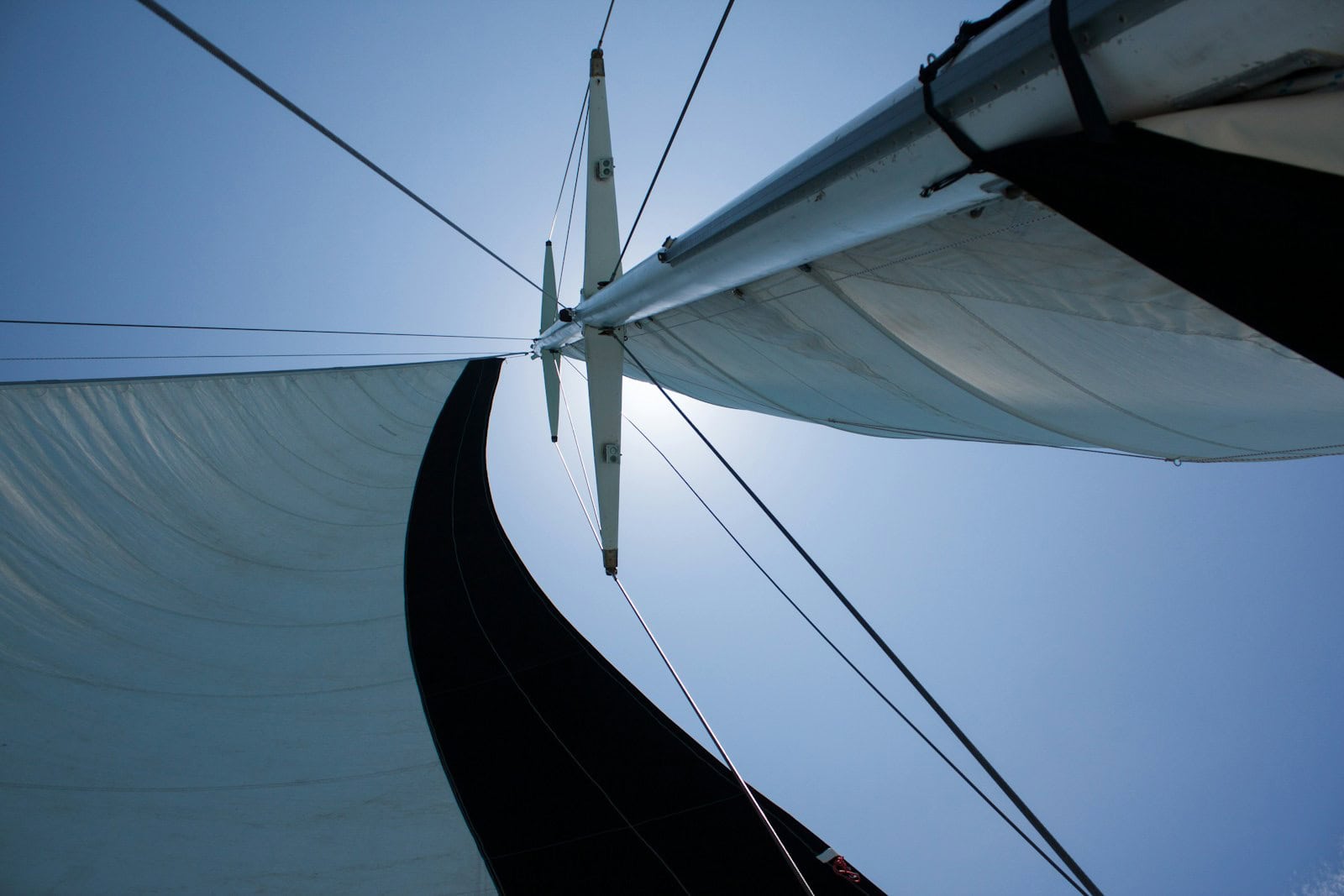 Blick von unten auf Mast und Segel eines Segelboots vor blauem Himmel