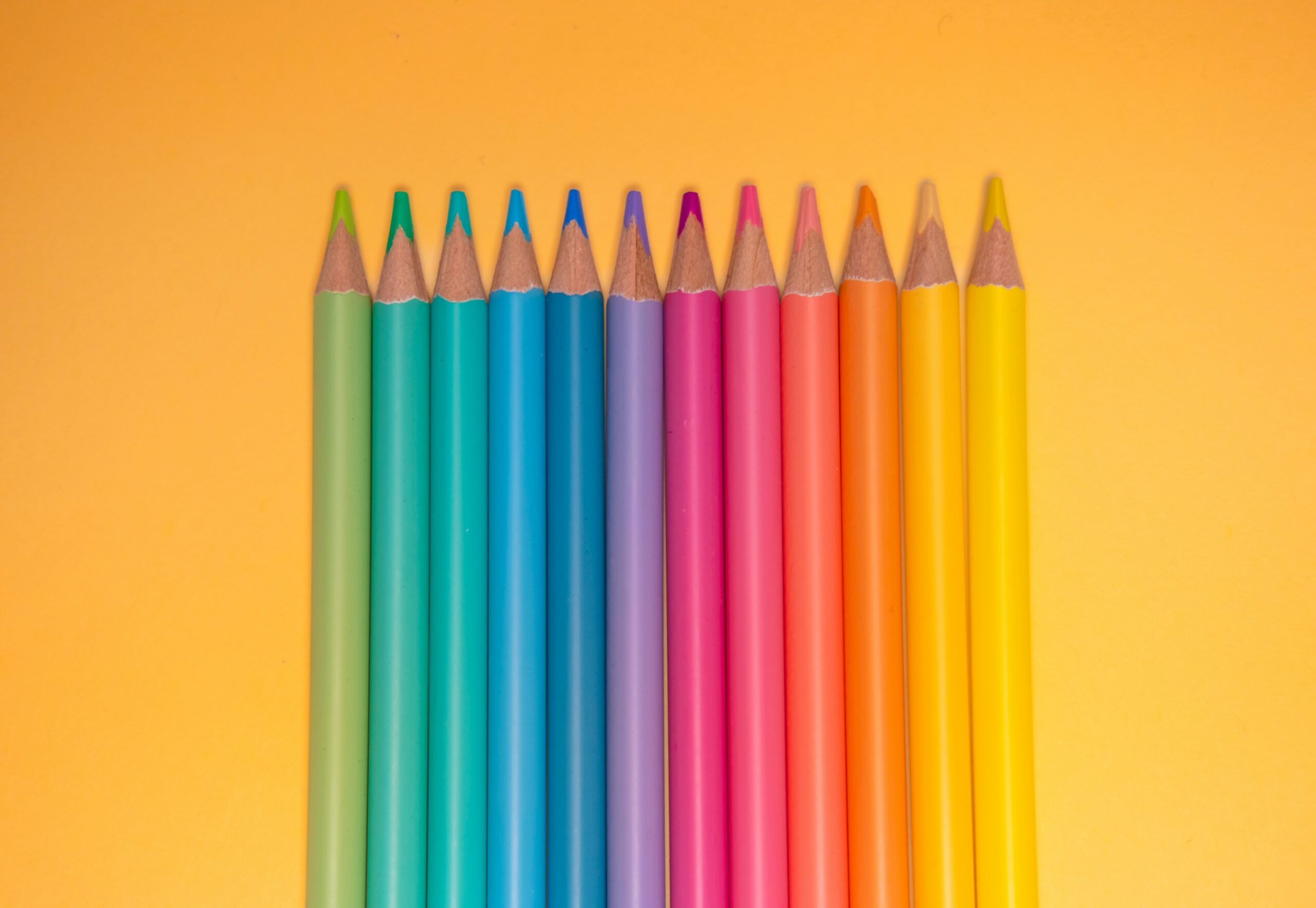 Reihe bunter Buntstifte in Pastellfarben auf orangem Hintergrund